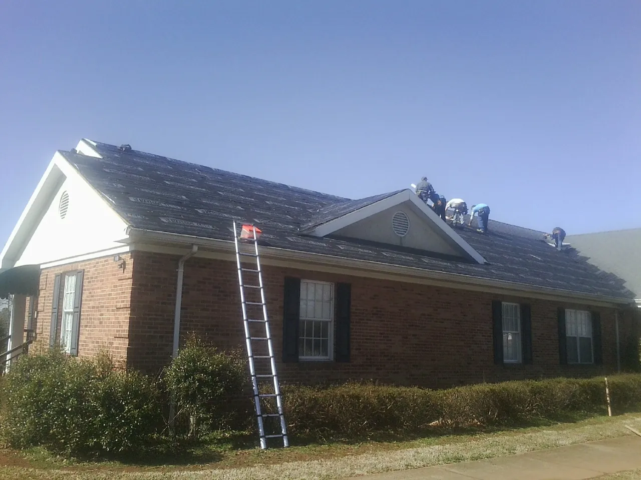 Crew tearing shingles off a brick ranch roof with a ladder set — Emergency Roof Repair work by our crew in Orting