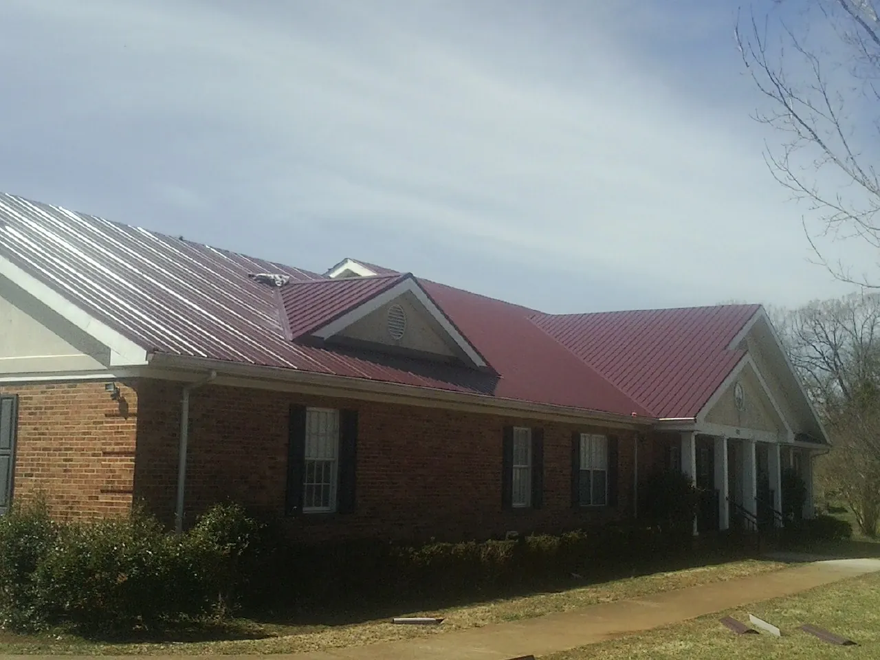 Red metal roof with gabled entries on a long brick building, from a Hail Damage Roof Repair job in Orting