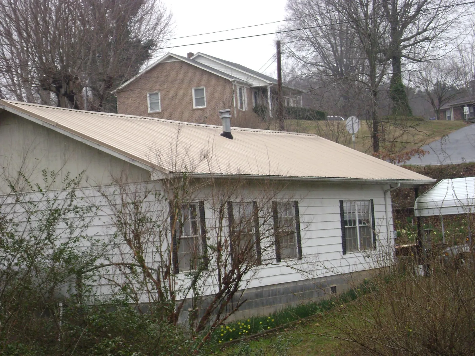 Tan metal roof on a white sided house set into a hillside — Commercial Roofing by Roofing Brothers in Orting